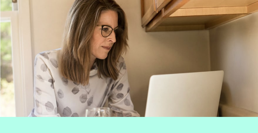 Dunkelblonde Frau mit Brille und weißem Langarm T-Shirt schaut konzentriert in ihren grauen Laptop.